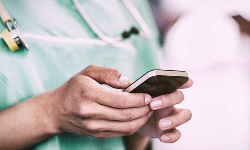 Dokter dan perawat meninjau rincian jasa pelayanan pada ponsel di area klinis, memperlihatkan transparansi poin tindakan dan konversi rupiah tanpa klaim absolut.